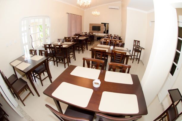 Uma sala de jantar vazia com mesas e cadeiras marrons dispostas para o serviço. Sobre as mesas, há jogos americanos bege suaves.