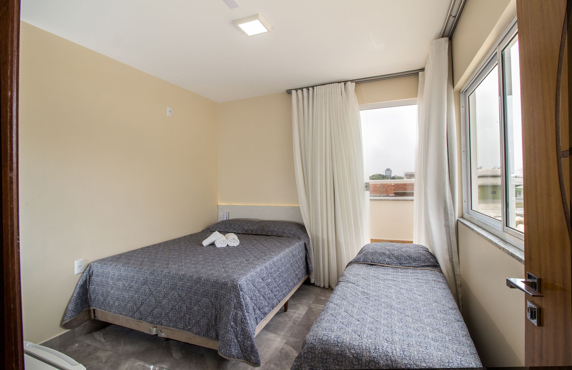 Um pequeno quarto de hotel com duas camas de solteiro cobertas com cobertores estampados em cinza e branco.