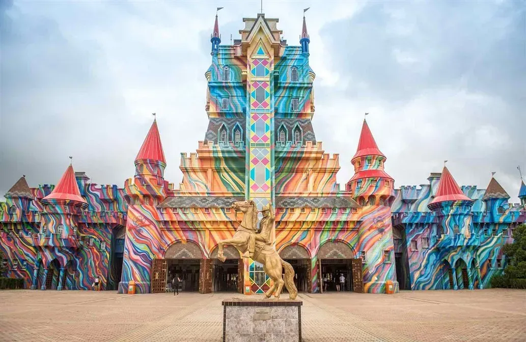 Um castelo colorido e psicodélico com uma estátua dourada na fachada. O edifício tem várias torres e um redemoinho de tinta brilhante.