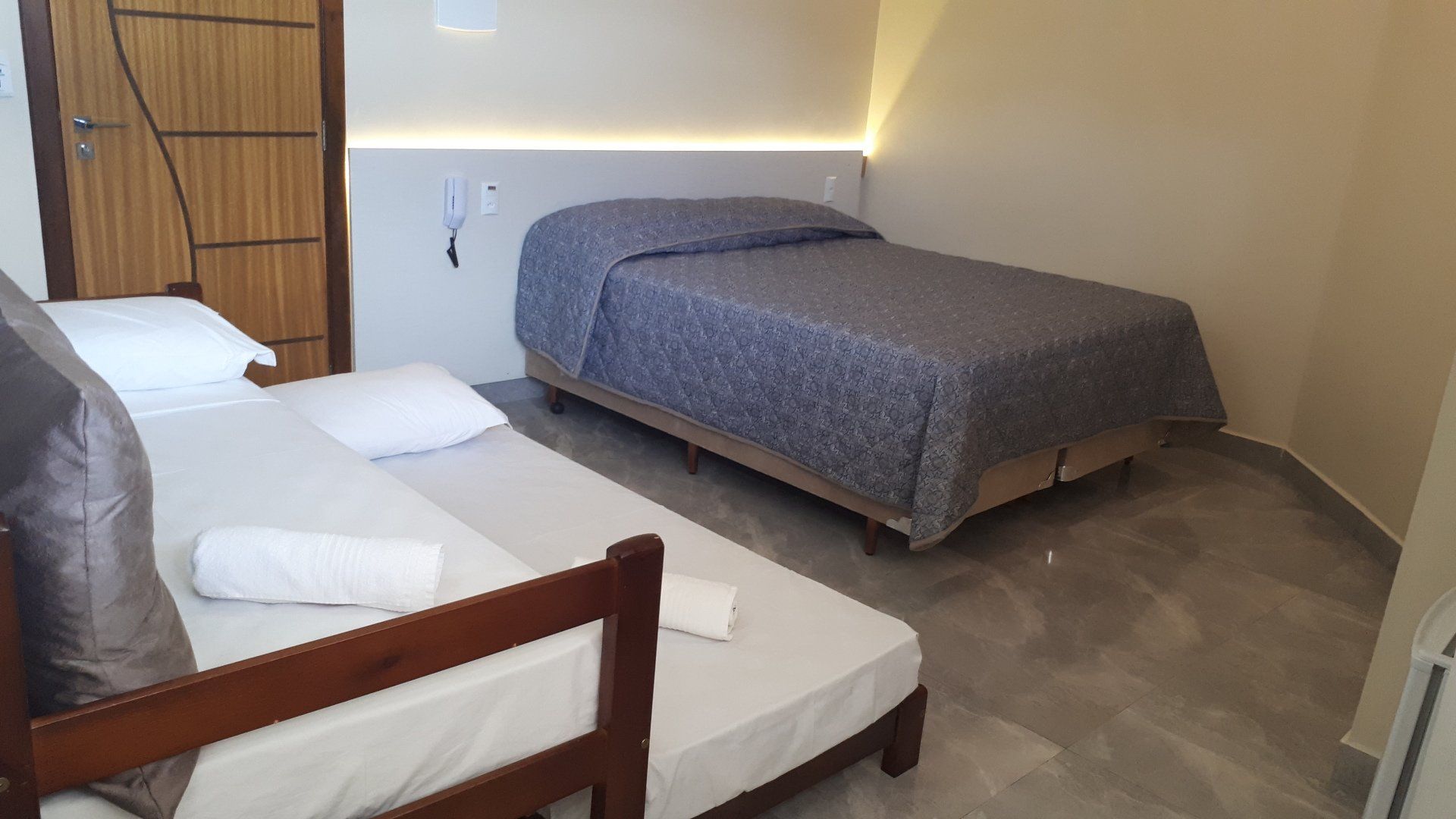 Um pequeno quarto de hotel com uma cama de casal e um sofá-cama, com paredes neutras e detalhes em madeira.