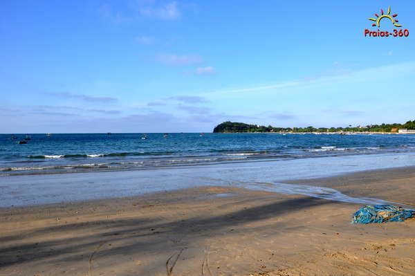 Cena de praia com céu azul claro, oceano calmo, praia arenosa e um pequeno pedaço de corda azul.