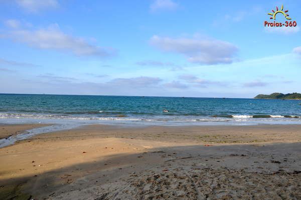 Cena de praia com oceano azul, praia arenosa e céu parcialmente nublado.
