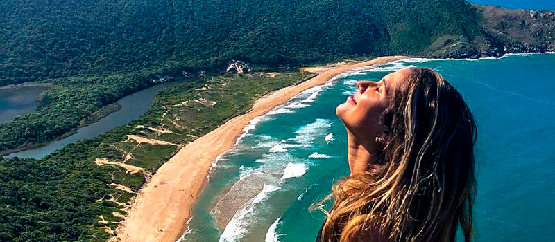 Uma mulher está no topo de uma colina com vista para uma praia.