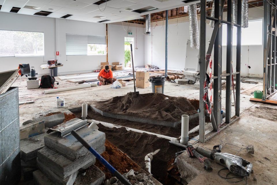 A Man is Digging a Hole in the Floor of a Building Under Construction — Moltus Construction in Braddon, ACT