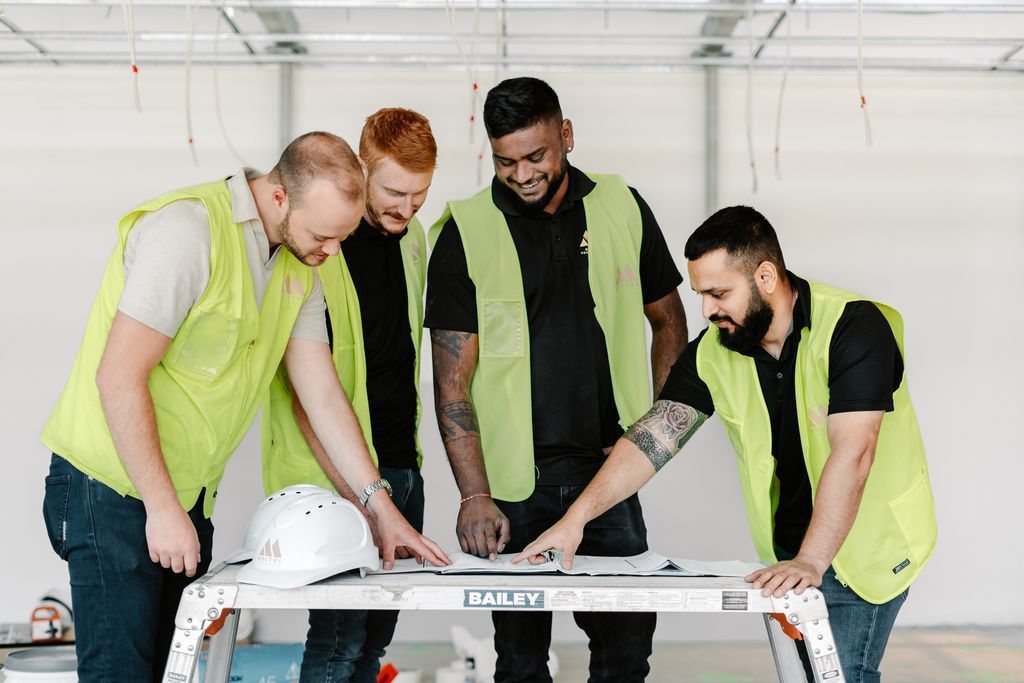 A Group of Construction Workers Are Standing Around a Table — Moltus Construction in Braddon, ACT