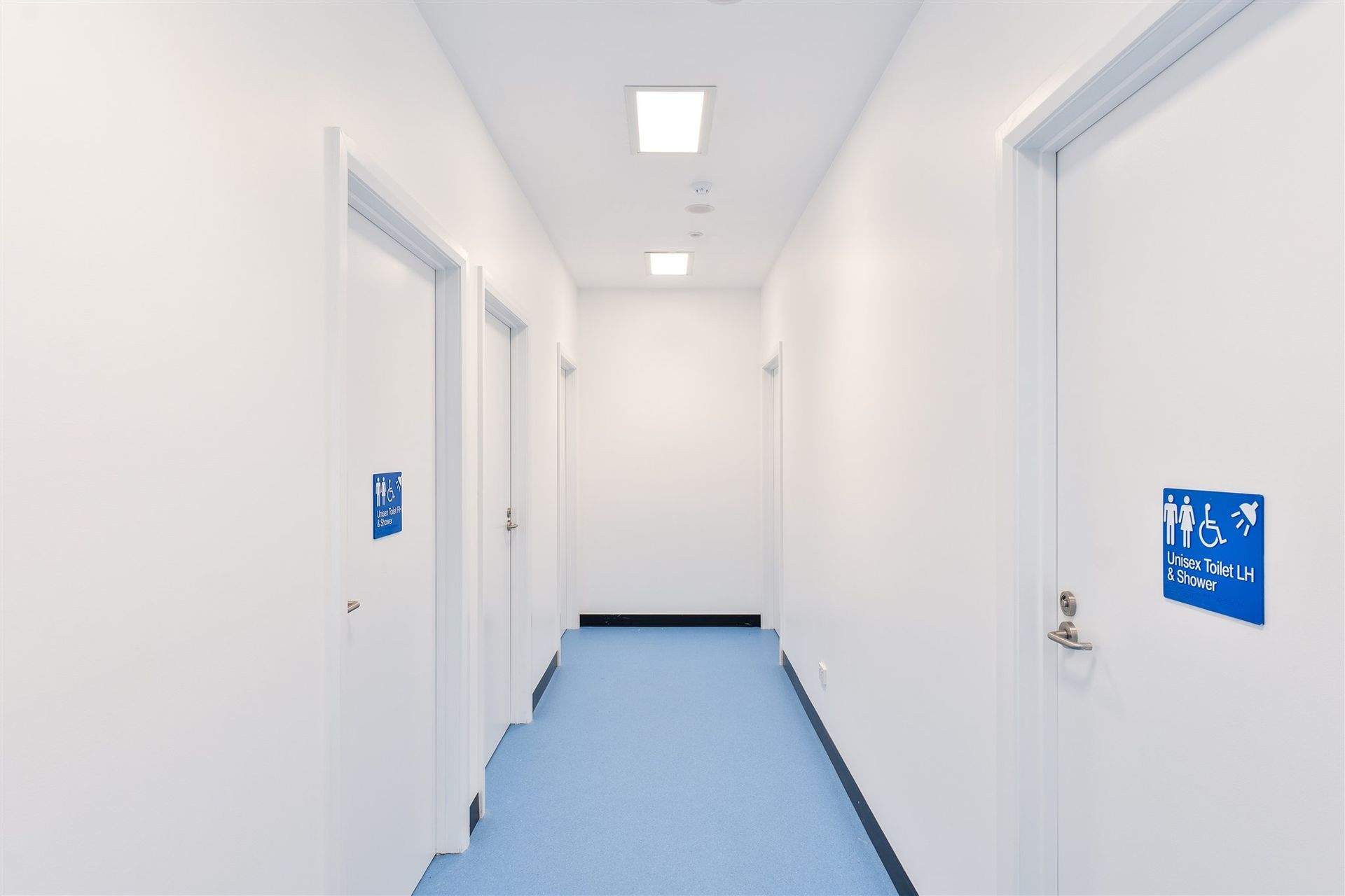 A Long Hallway With Blue Floors and White Doors in a Hospital — Moltus Construction in Braddon,  ACT