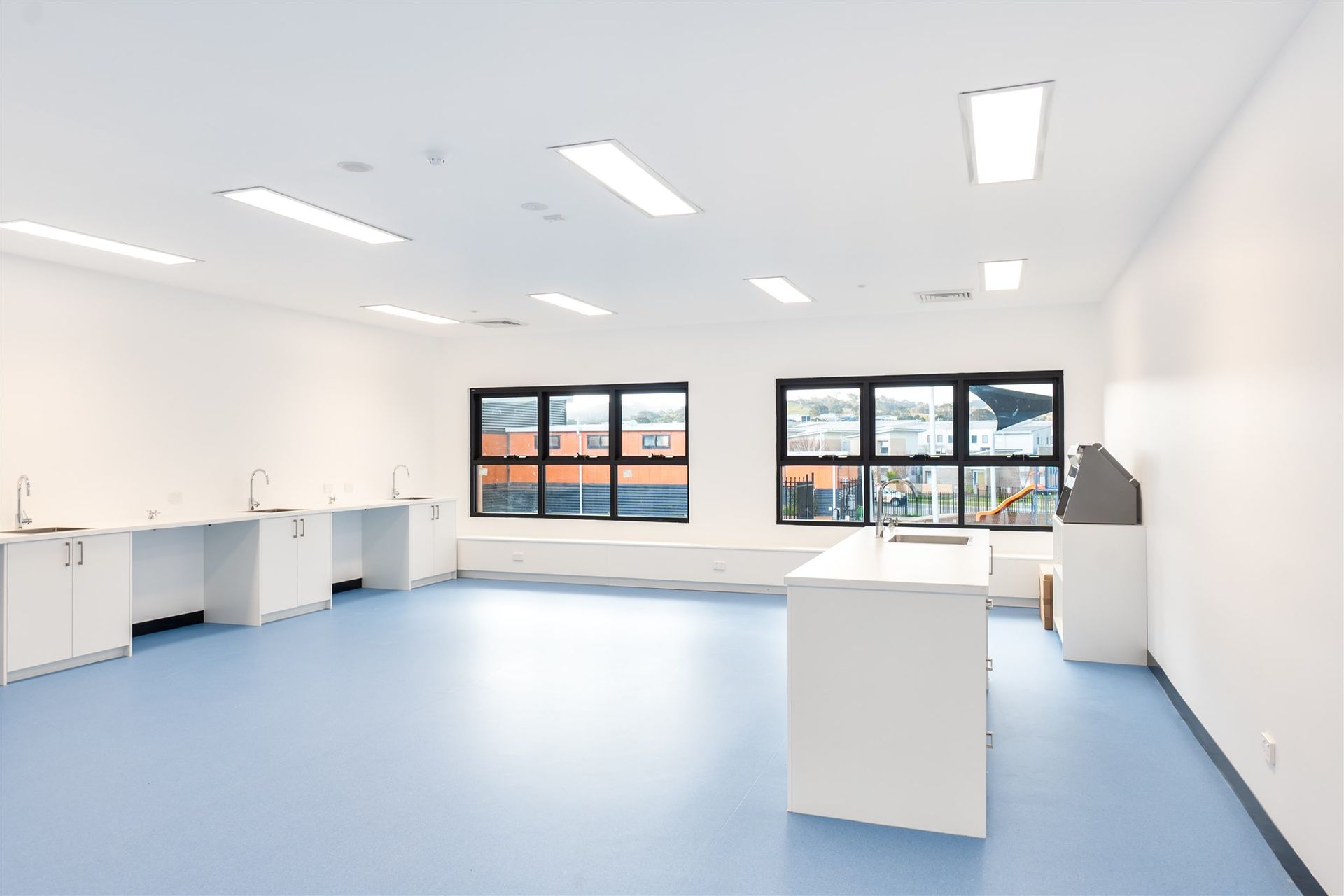 A Large Empty Room With Blue Floors and White Cabinets — Moltus Construction in Braddon,  ACT