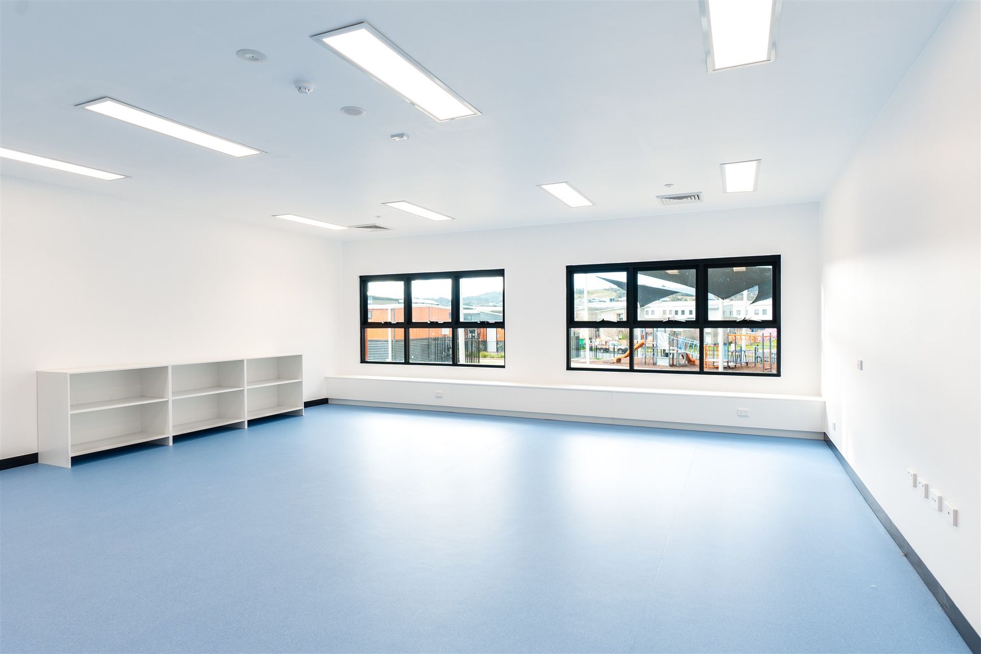 A Large Empty Room With Blue Floors and White Walls — Moltus Construction in Braddon,  ACT