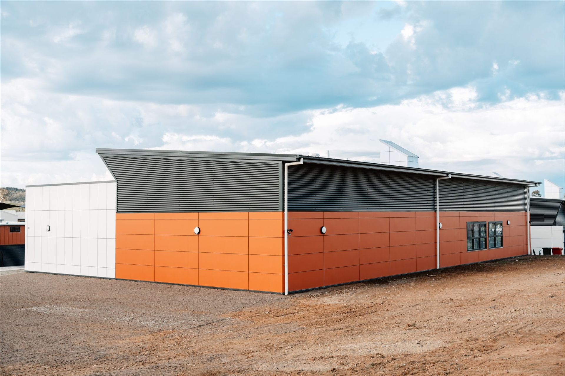 A Large Building With Orange and Black Walls is Sitting in the Middle of a Dirt Field — Moltus Construction in Braddon,  ACT