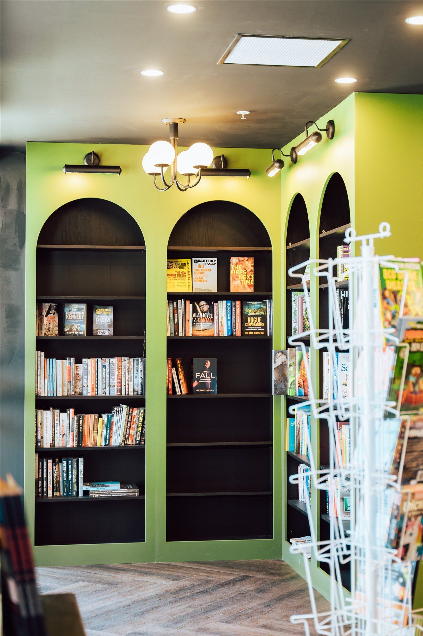 A Bookstore With Green Walls and Black Shelves Filled With Books — Moltus Construction in Braddon, ACT