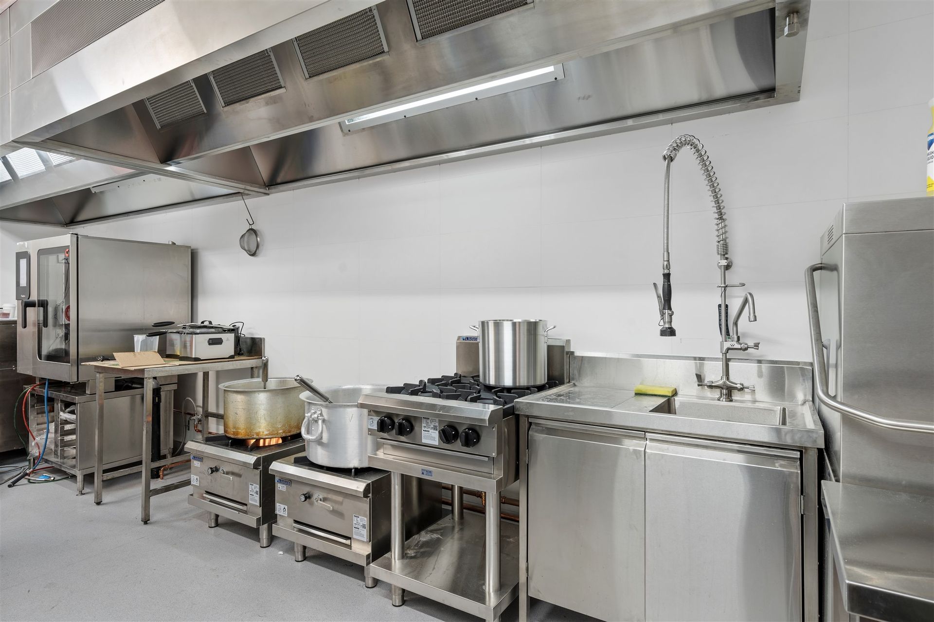 A kitchen with stainless steel appliances, pots and pans, and a sink — Moltus Construction in Braddon,  ACT