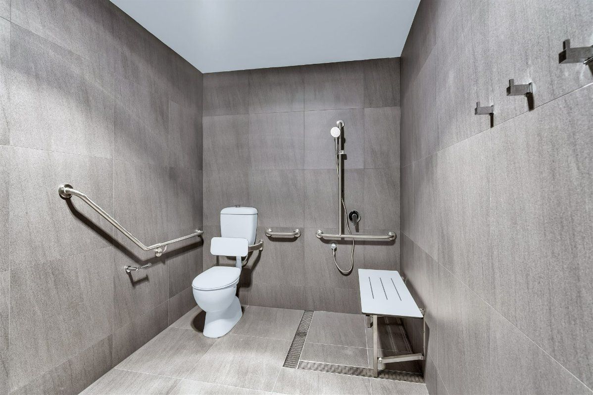 A Handicapped Bathroom With a Toilet, Shower and Bench — Moltus Construction in Braddon,  ACT
