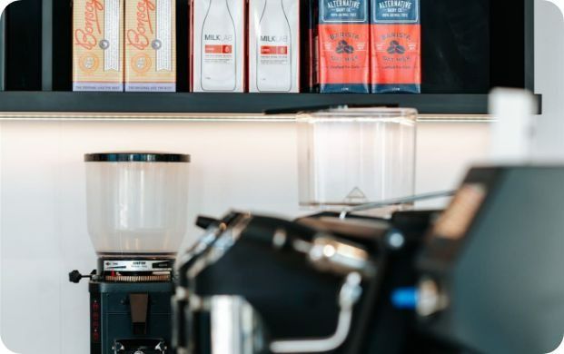 A Coffee Grinder is Sitting in Front of a Shelf With Boxes of Milk on It — Moltus Construction in Braddon,  ACT