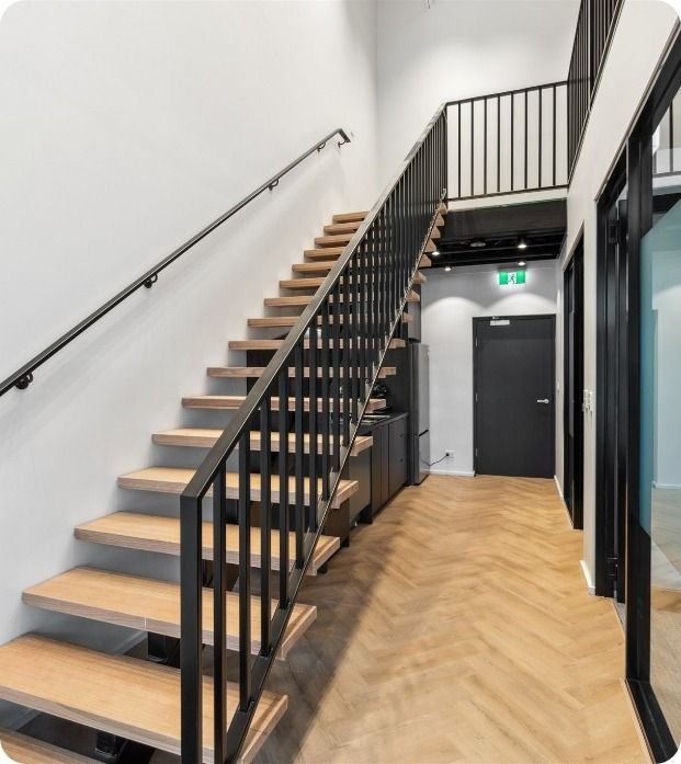 A Wooden Staircase With a Black Railing in a Hallway — Moltus Construction in Braddon,  ACT