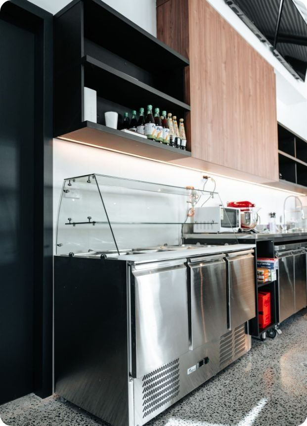 A Kitchen With Stainless Steel Appliances and Wooden Cabinets — Moltus Construction in Braddon,  ACT
