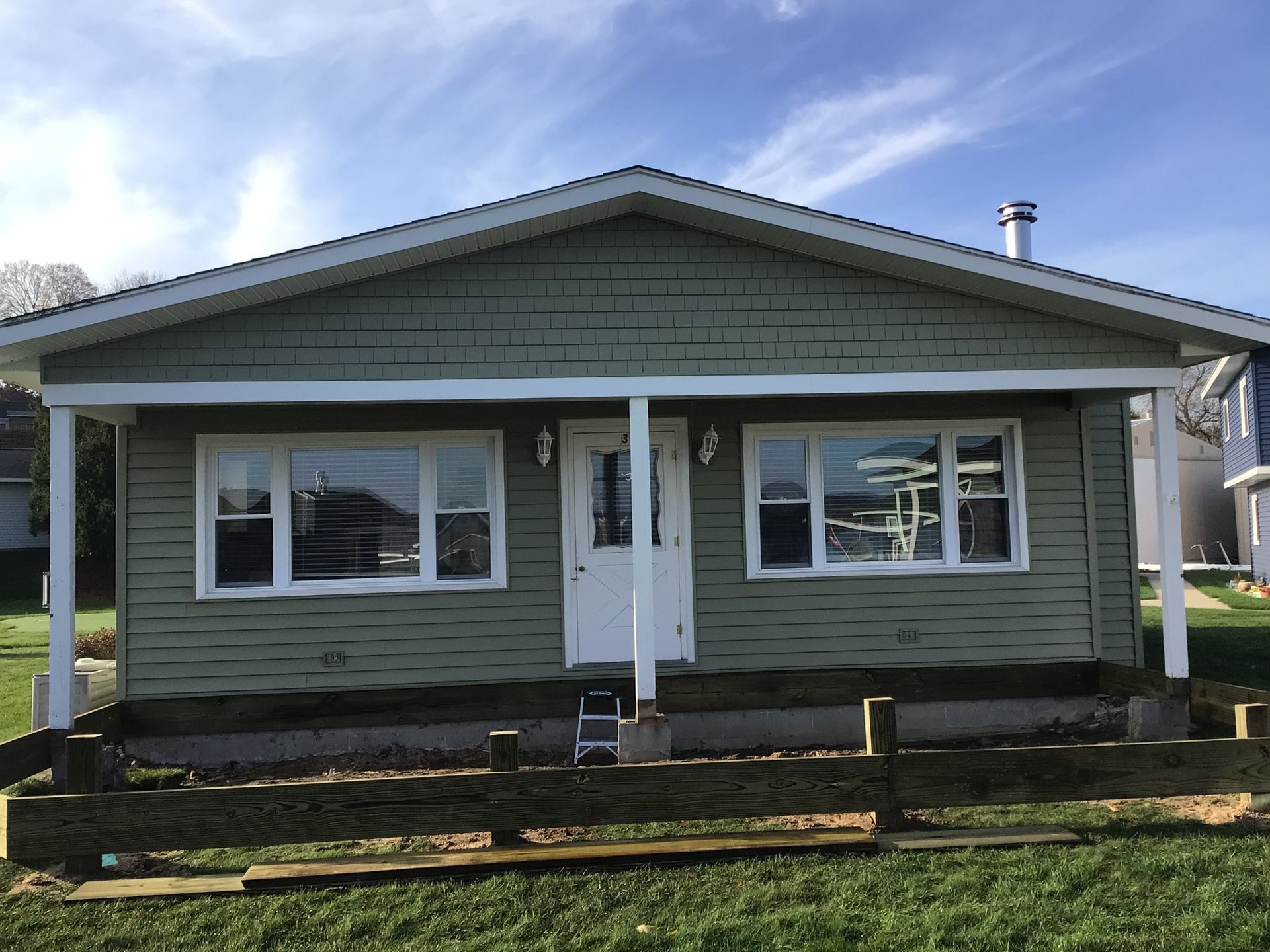 A small house with a porch and a fence in front of it.
