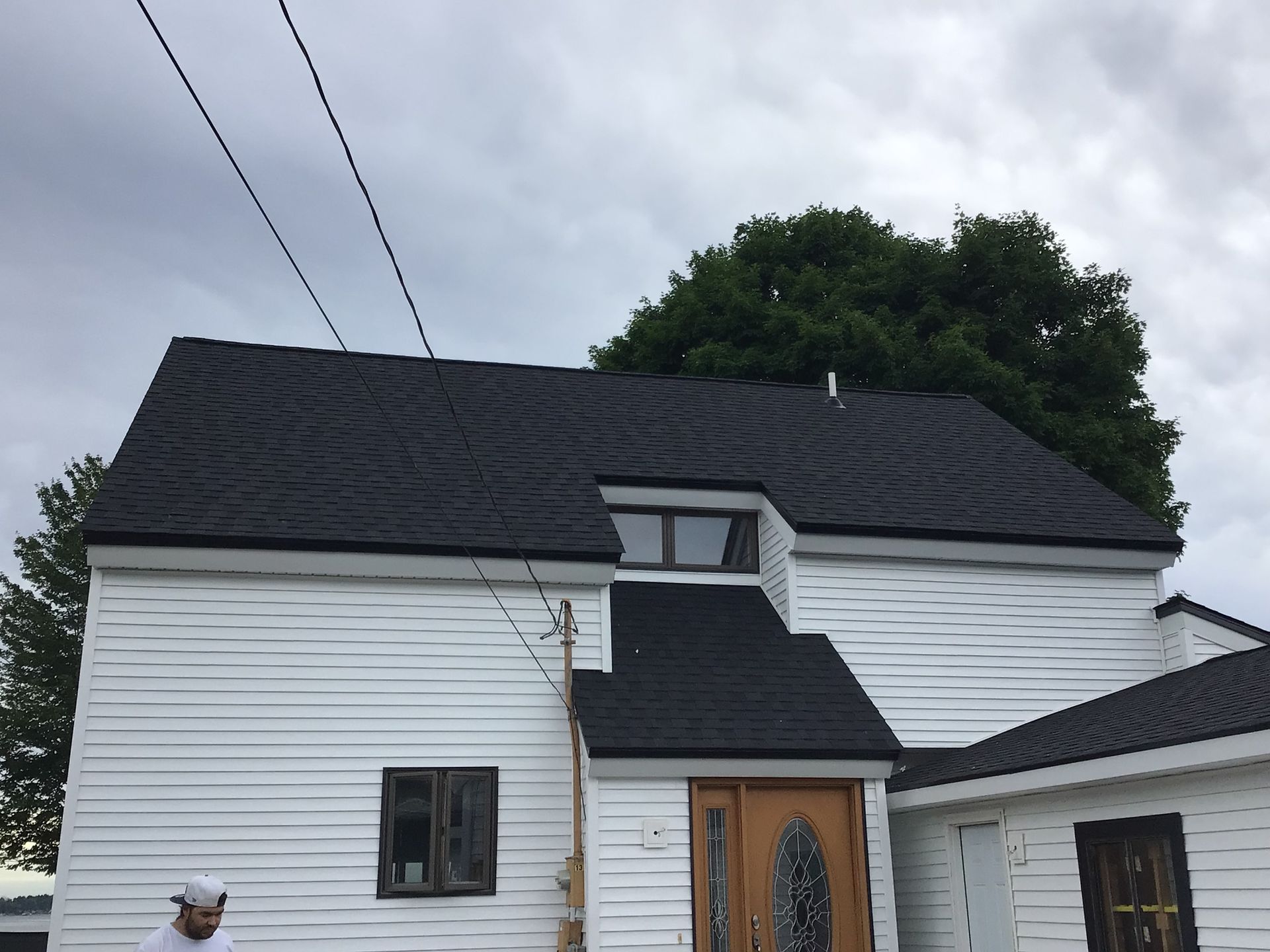A man is standing in front of a white house with a black roof.