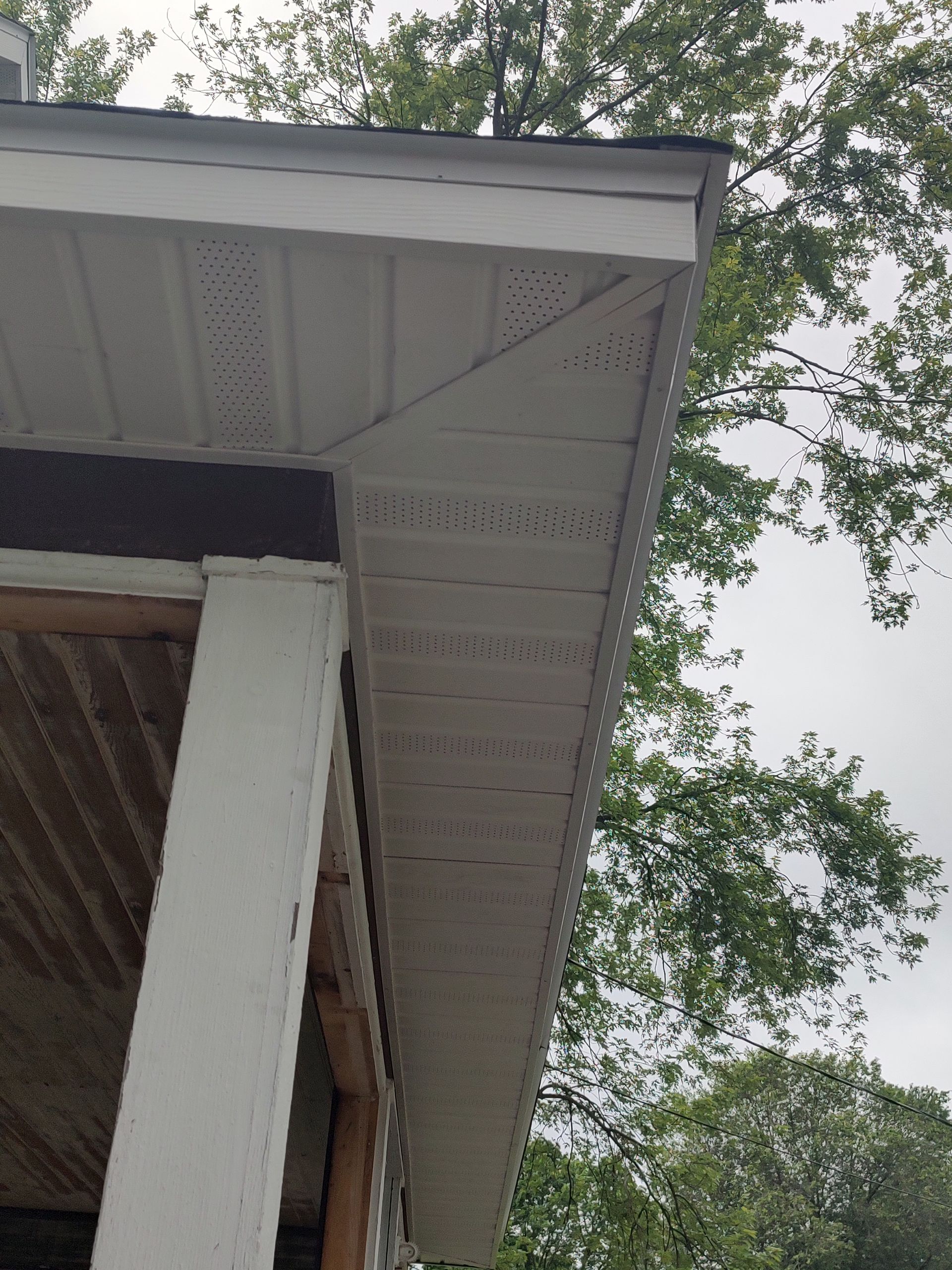 The roof of a house with a porch and trees in the background.
