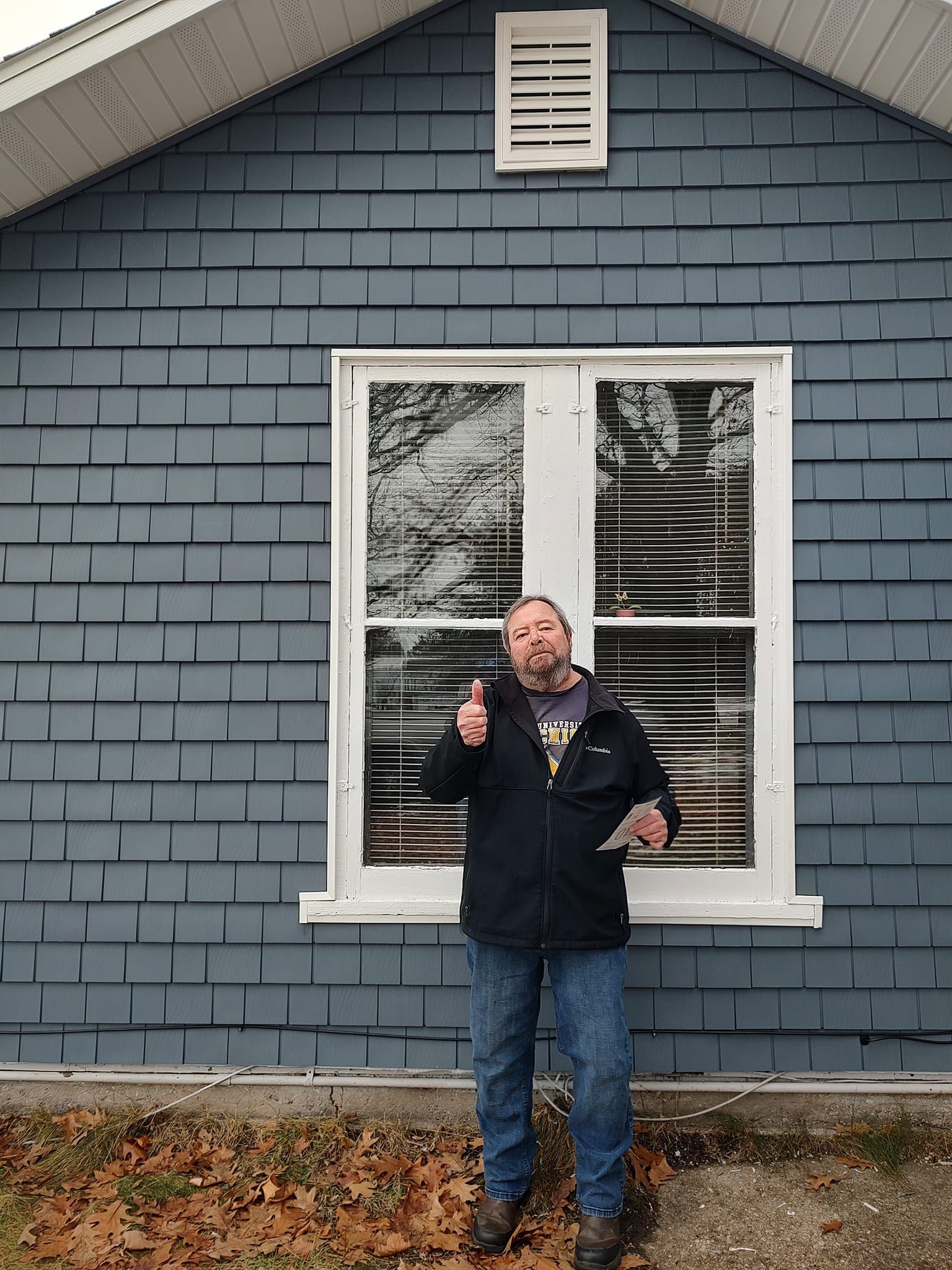 a man is standing in front of a blue house giving a thumbs up .