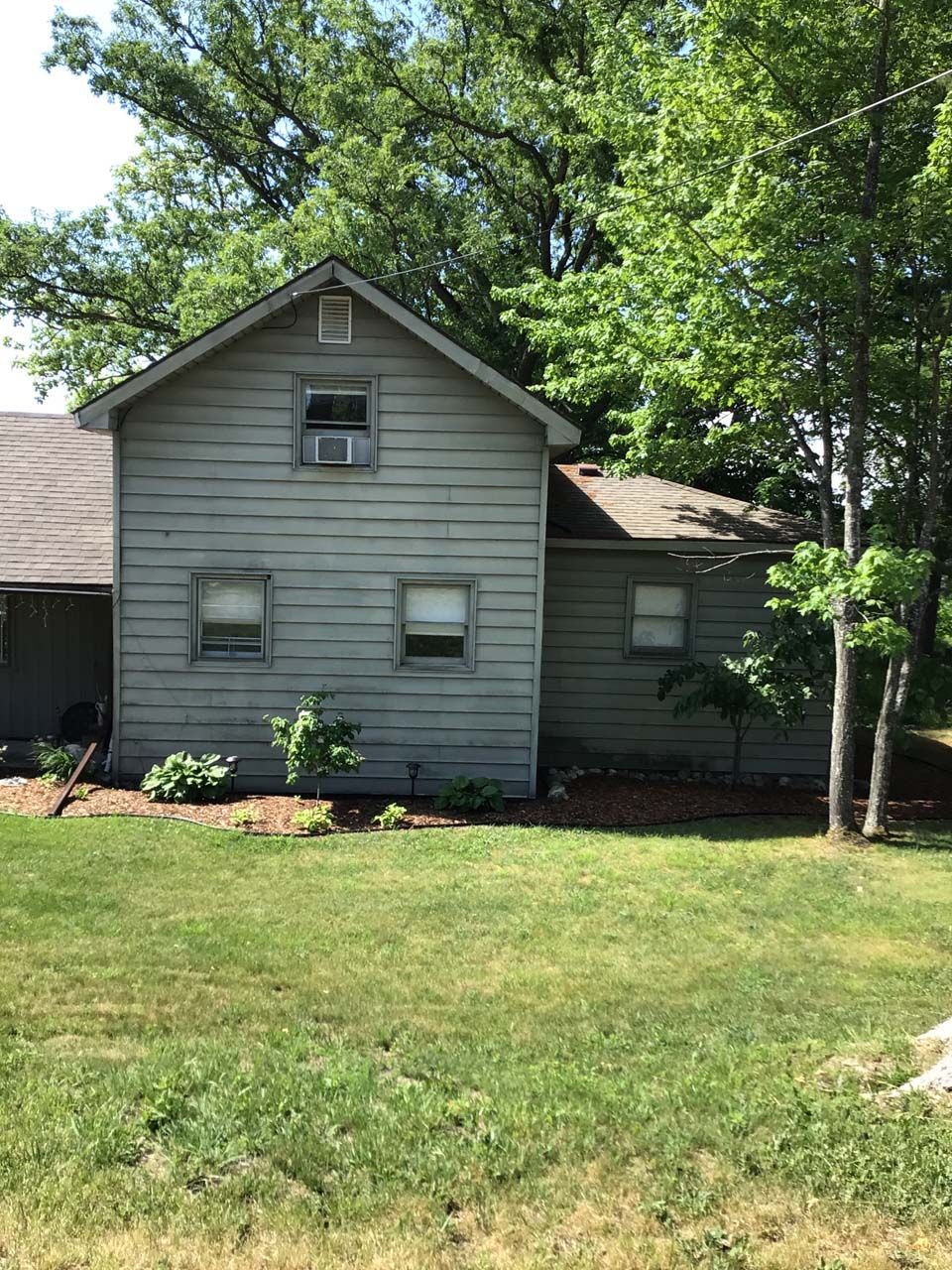 A house with a lot of windows is sitting in the middle of a lush green field.