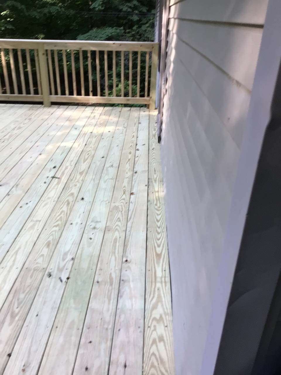 A wooden deck with a railing is next to a white house.