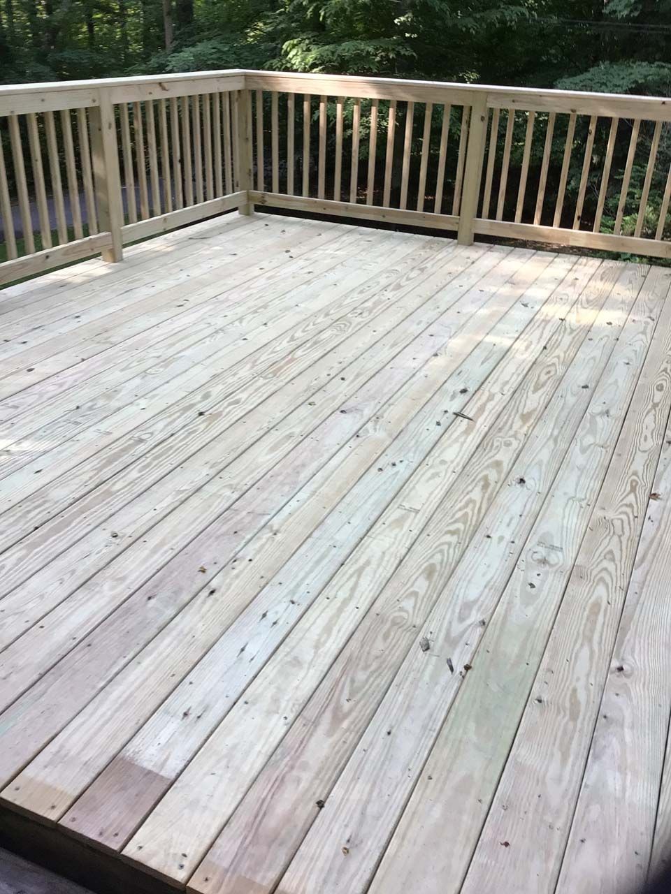 A wooden deck with a wooden railing and trees in the background.