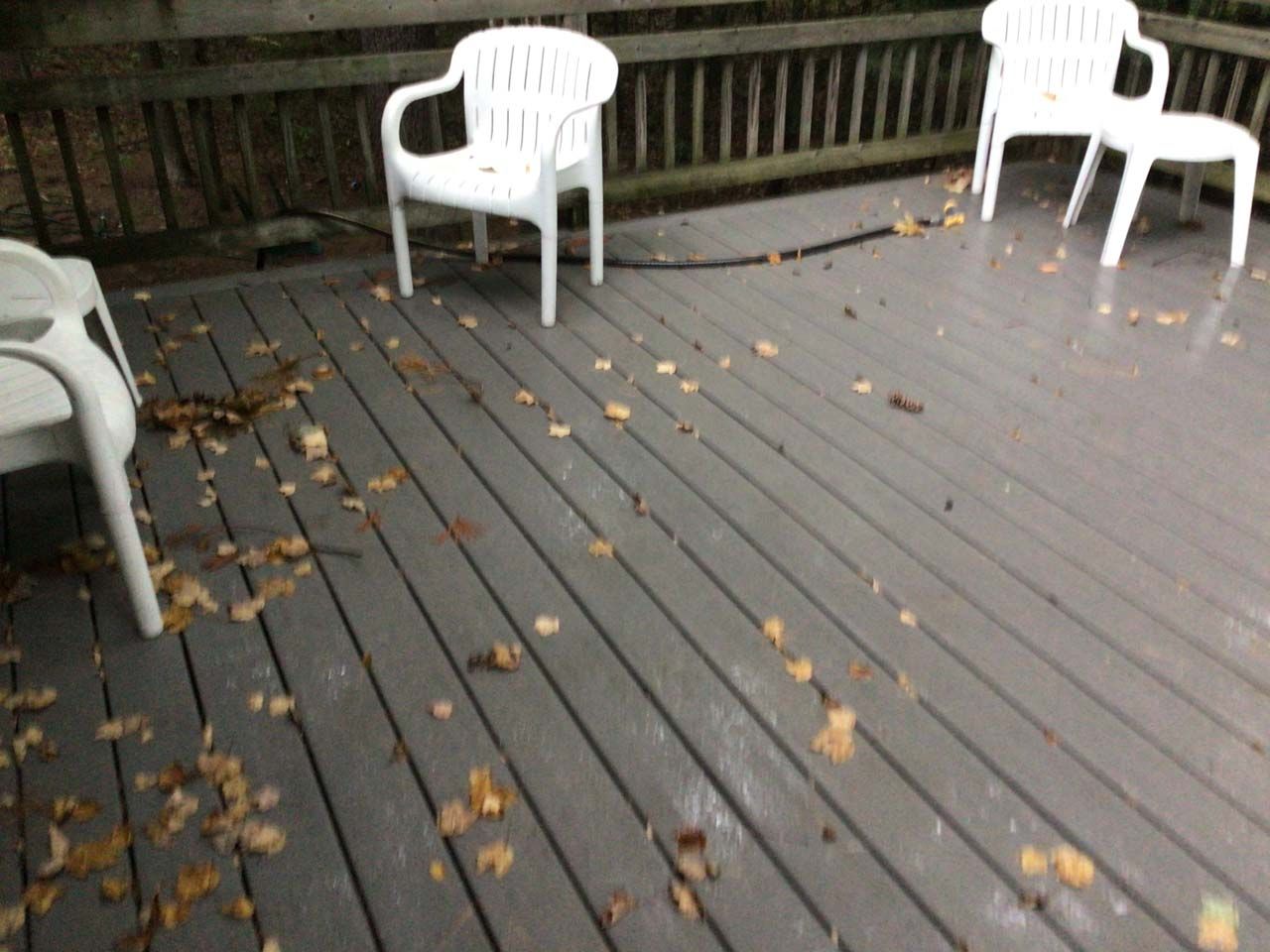 A deck with two white chairs and leaves on it