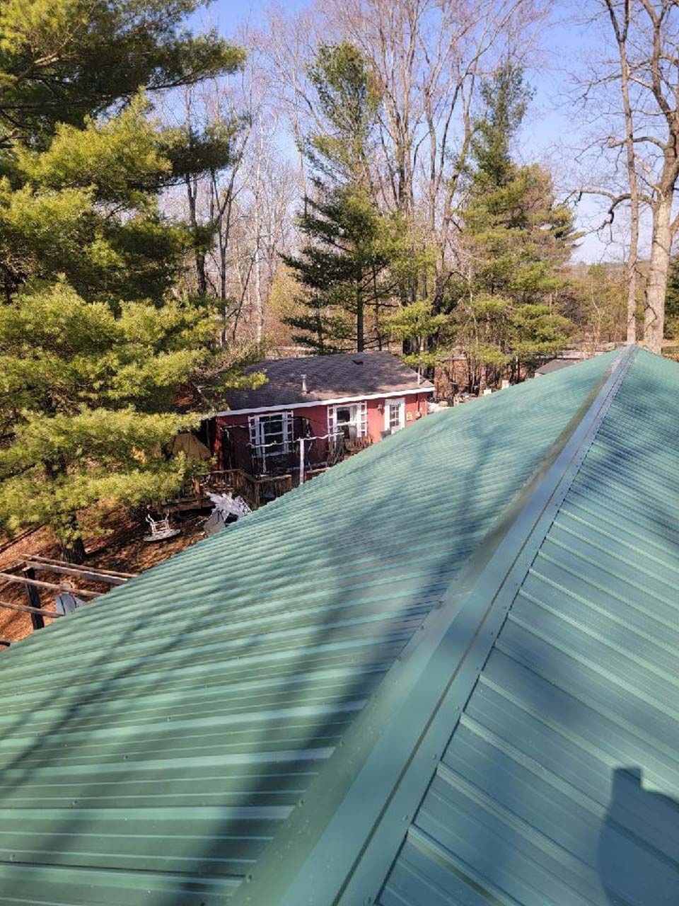 A green roof with a red house in the background is surrounded by trees.