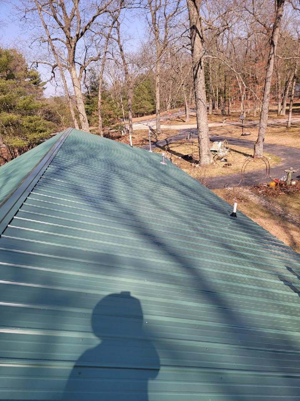 A green metal roof with a shadow of a person on it.