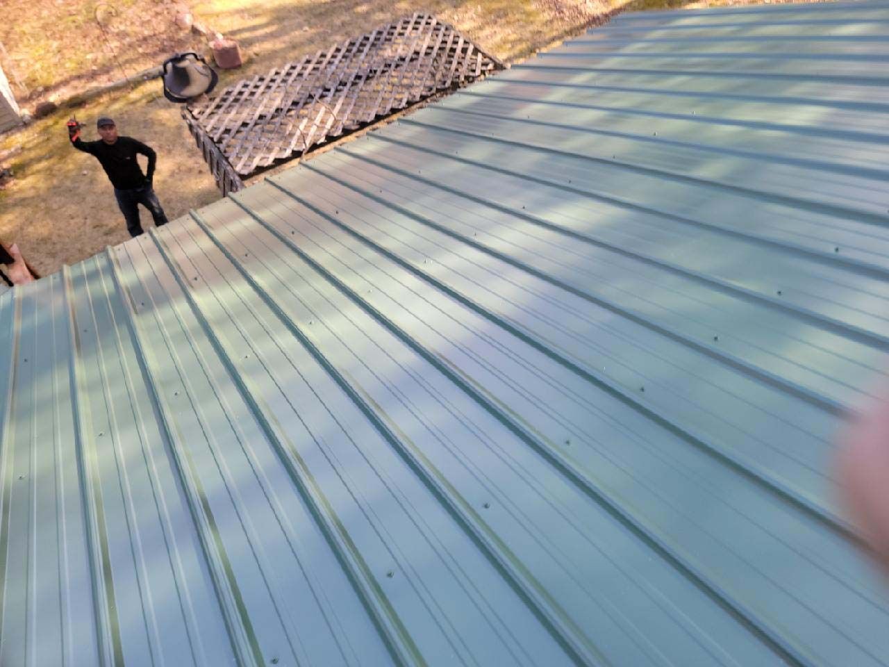 A man is standing on top of a green metal roof.