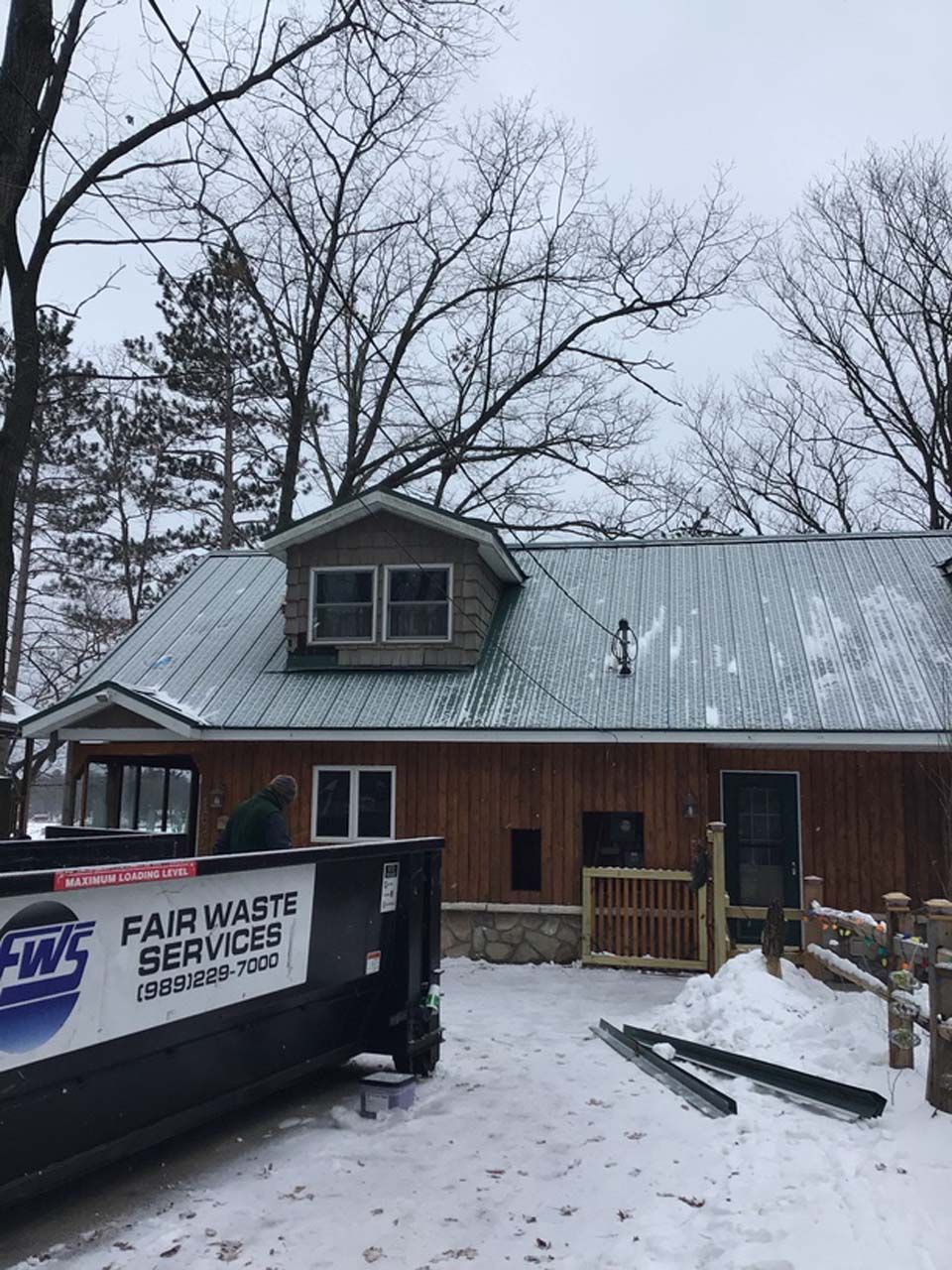 A dumpster is parked in front of a house in the snow.