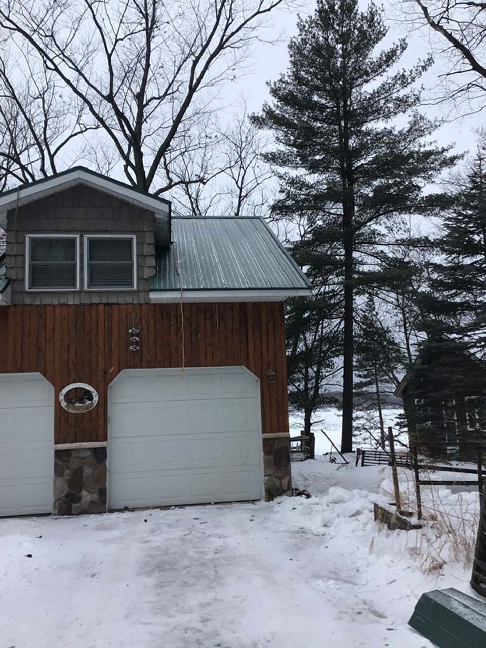 A garage with a green roof is surrounded by snow and trees.