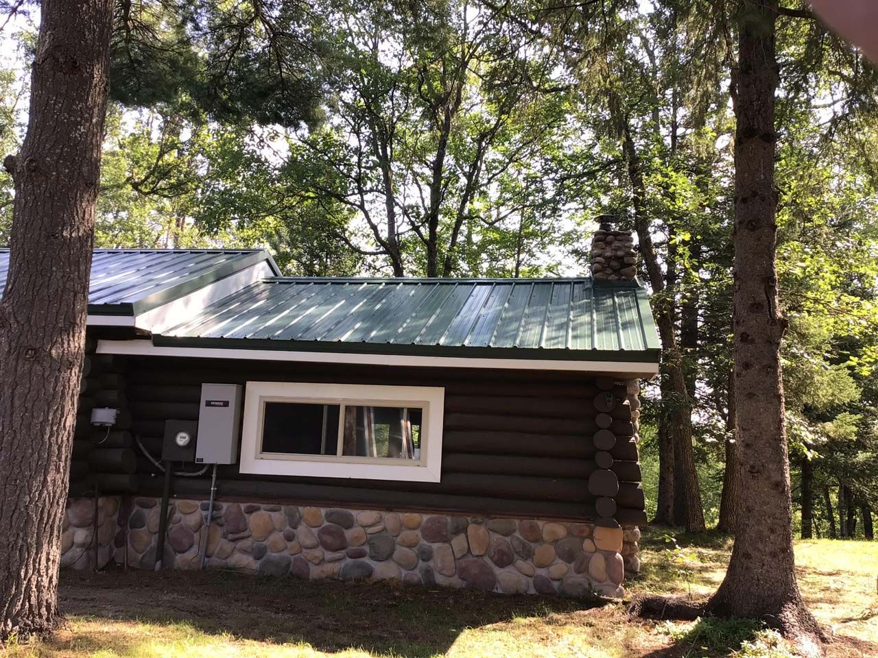 A log cabin with a green roof is surrounded by trees.