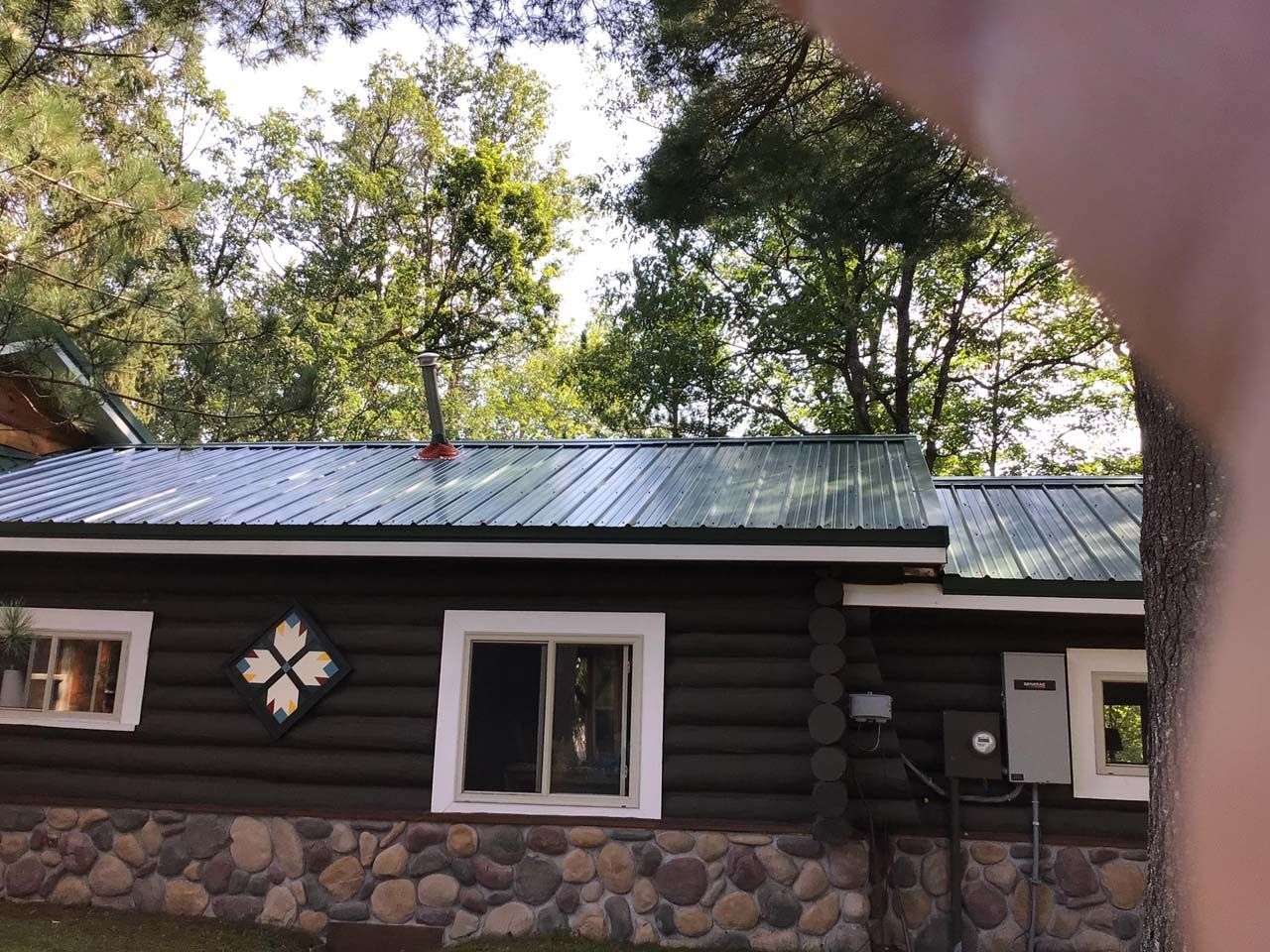 A person is pointing at a log cabin with a metal roof.