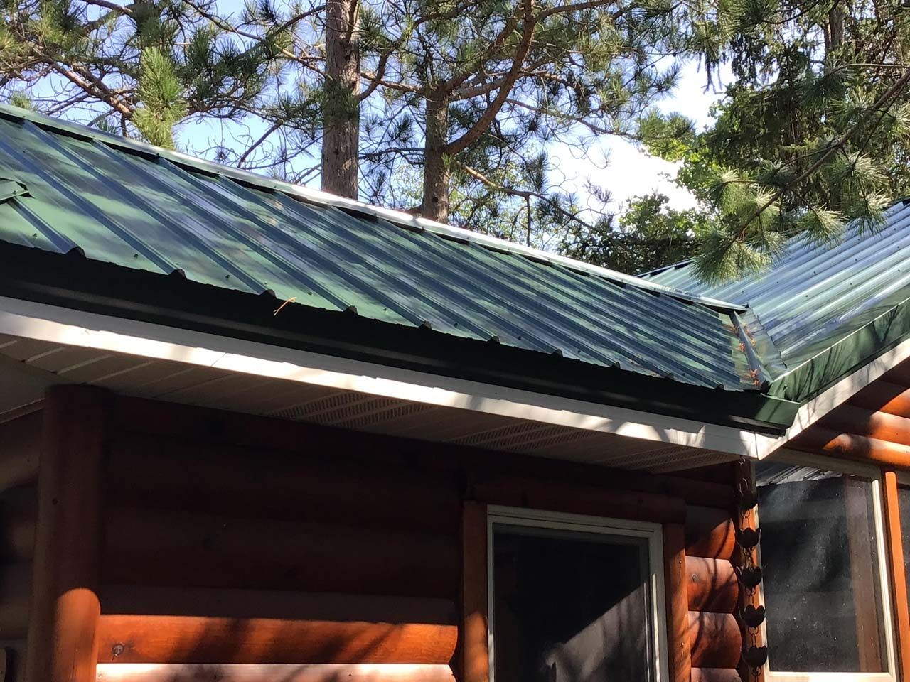 A log cabin with a green roof and trees in the background.