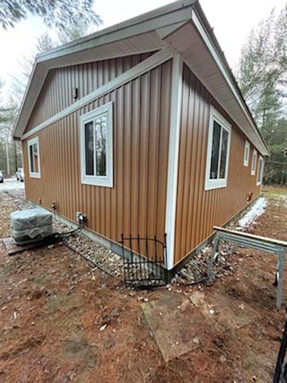 A brown house with white trim and windows is sitting in the middle of a dirt field.