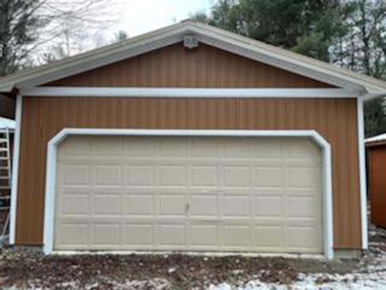 A garage with a tan garage door is sitting in the snow.