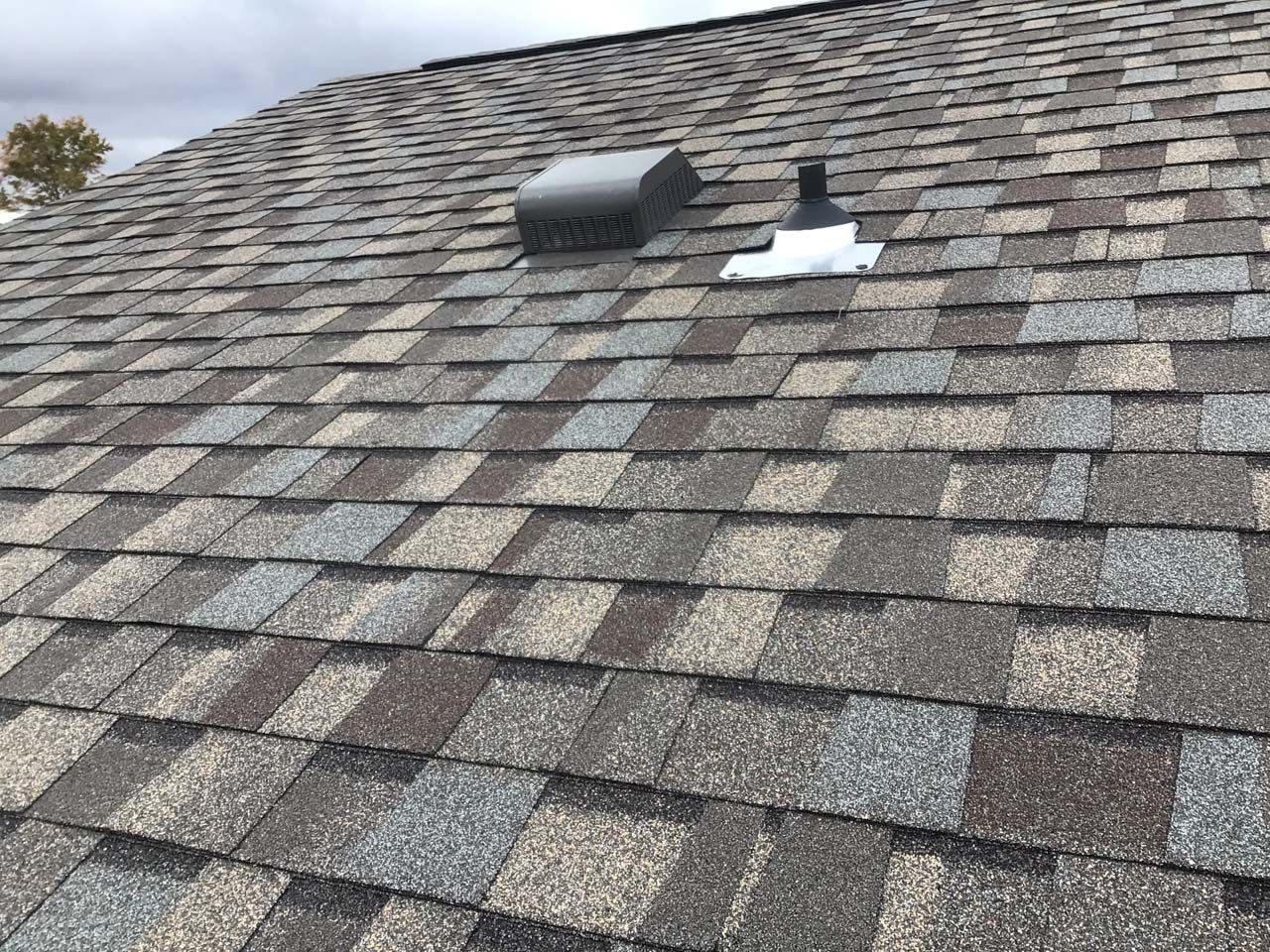 A close up of a roof with shingles and a vent on it.
