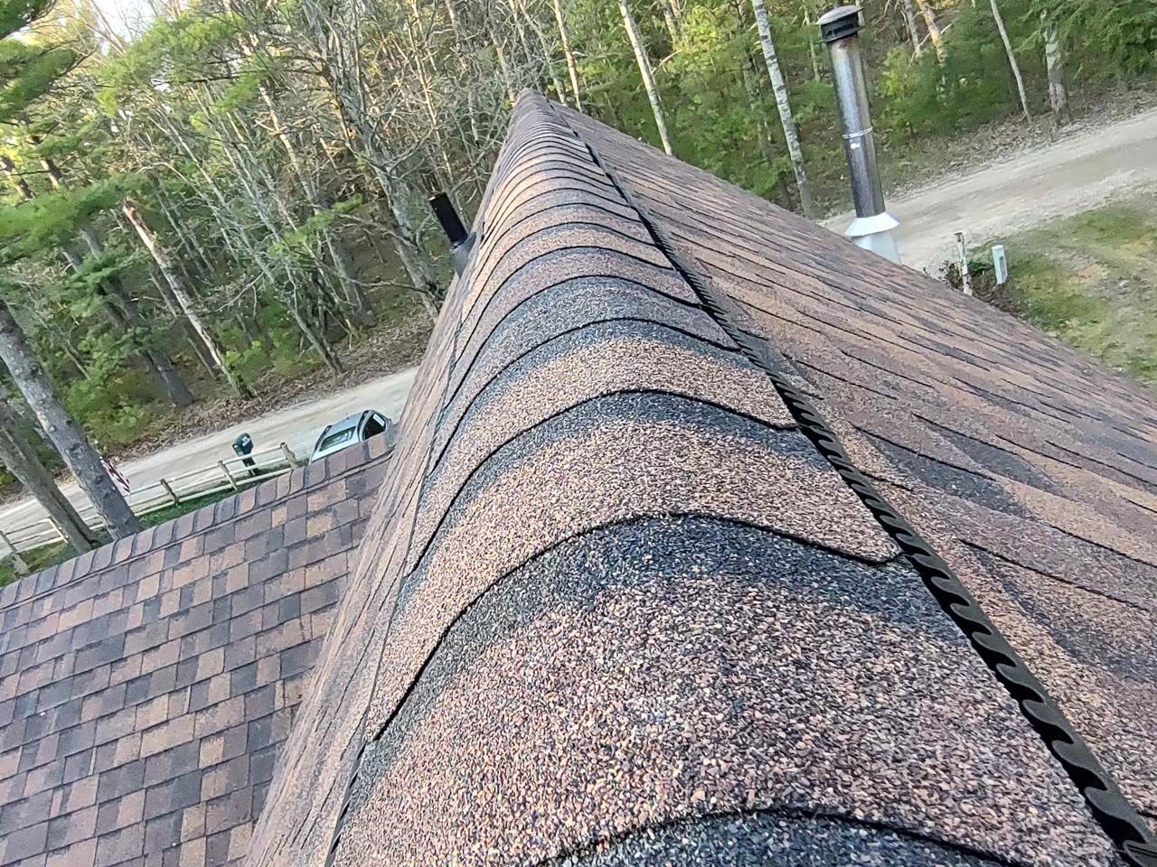 A close up of a roof with a chimney and trees in the background.