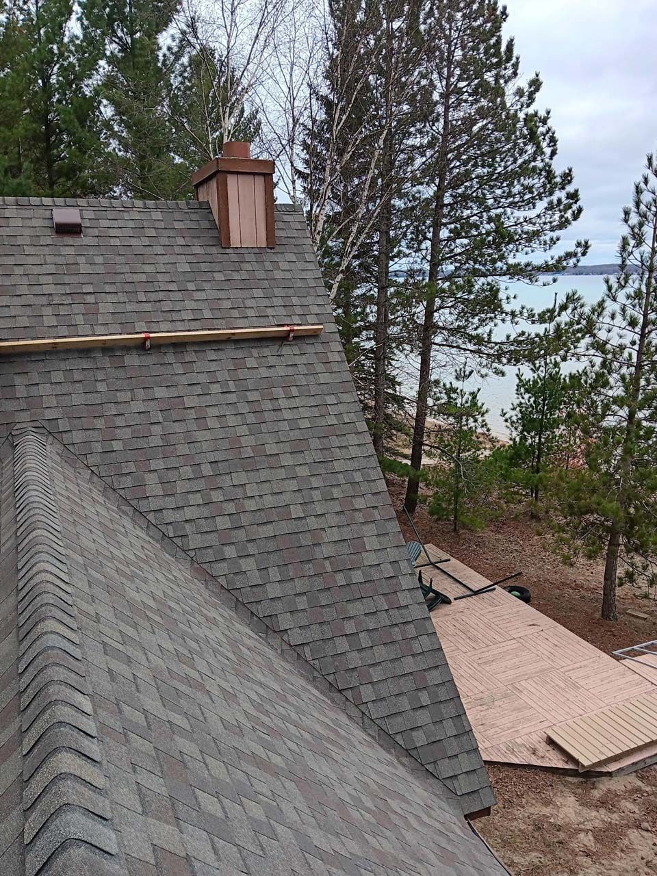 A roof with a chimney on top of it is surrounded by trees and a body of water.