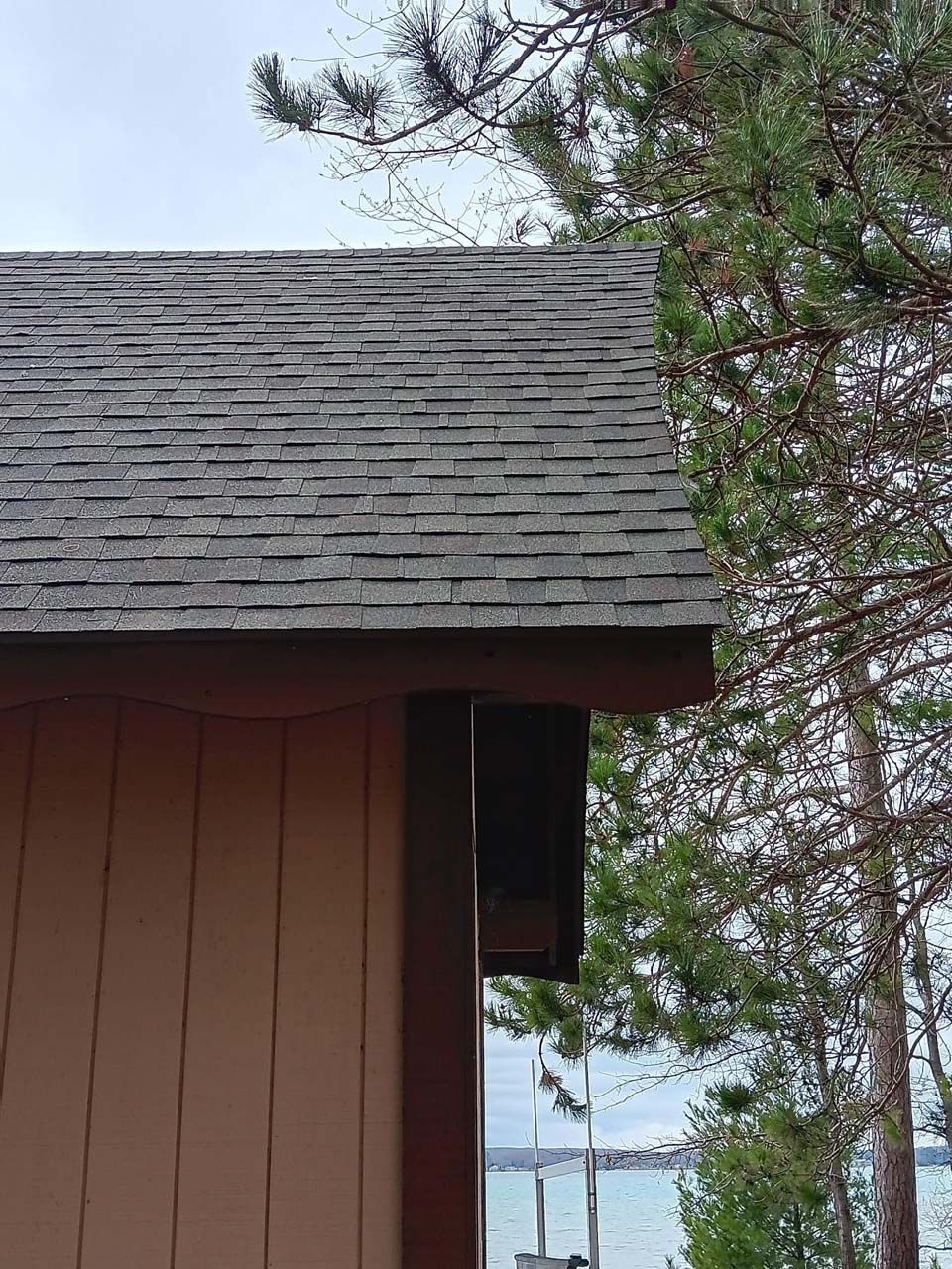 A house with a roof that is surrounded by trees and a body of water.