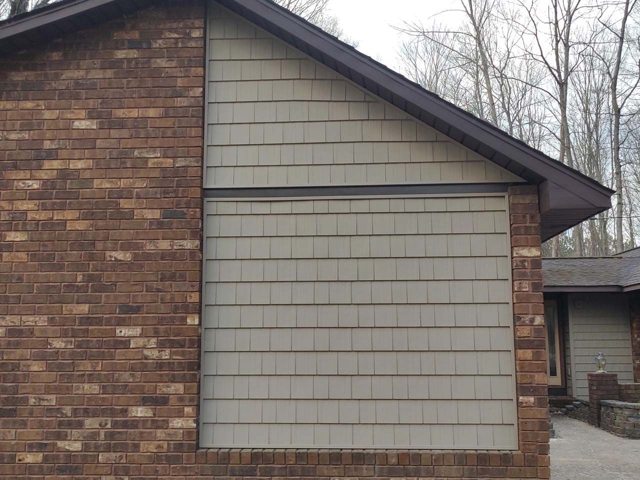 A brown brick house with a white siding on the side