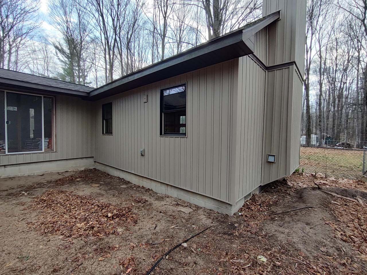 A house with a lot of windows is sitting in the middle of a forest.