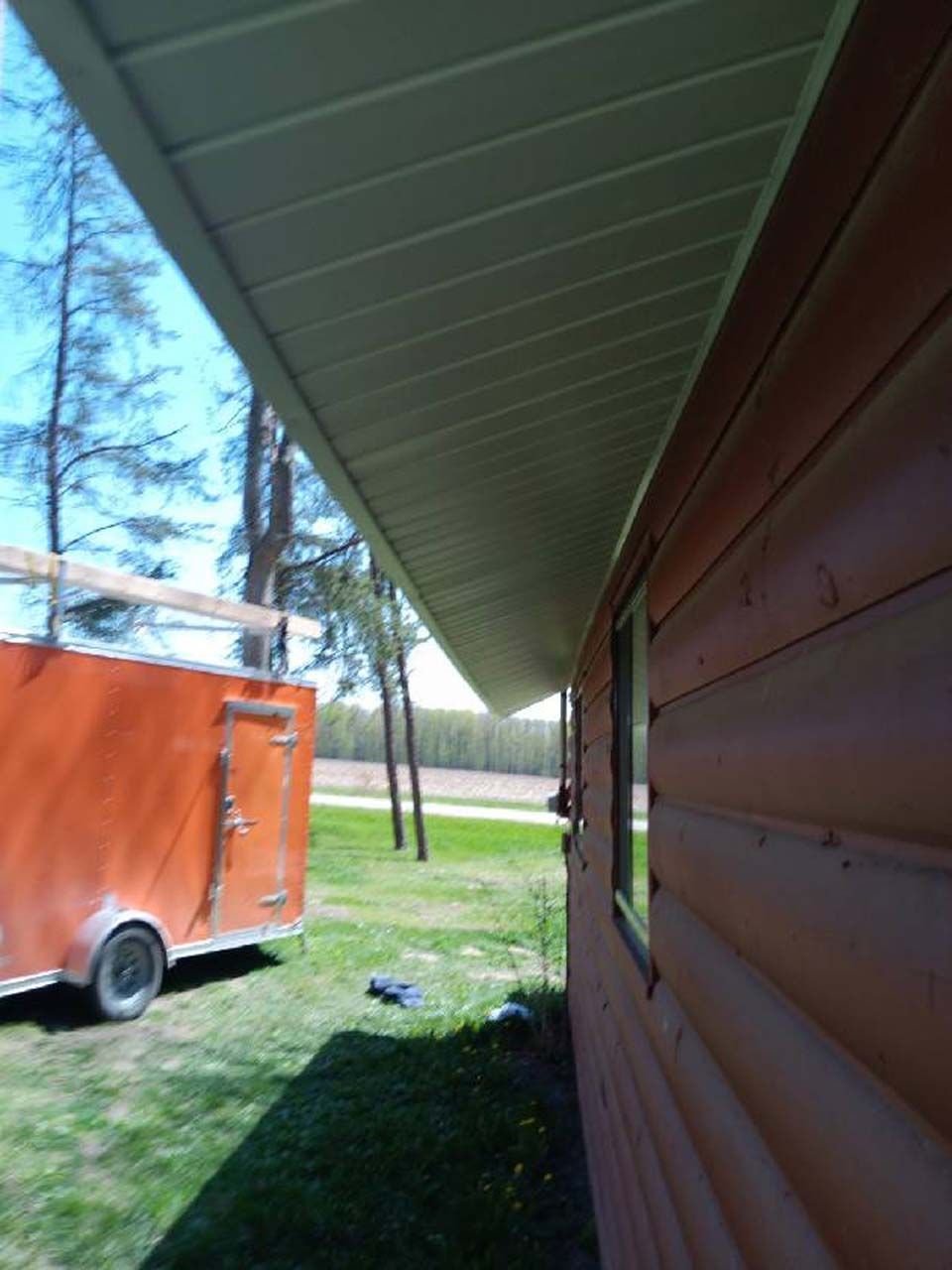 An orange trailer is parked under the roof of a house