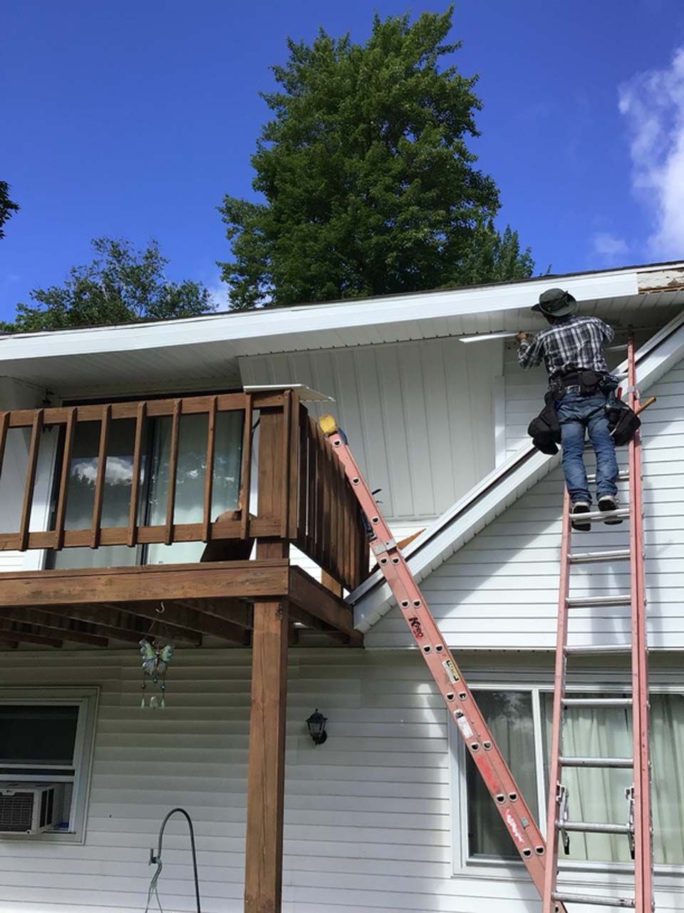 A man is standing on a ladder on the side of a house.