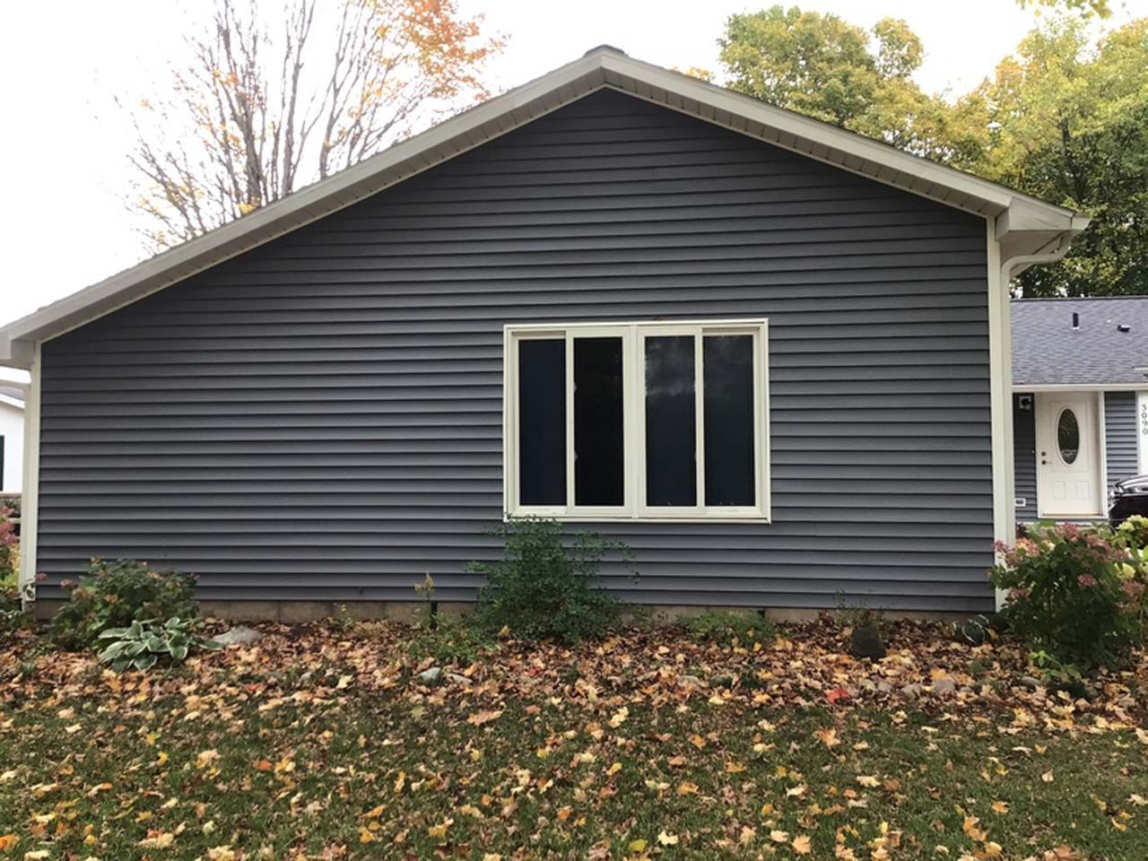 The back of a house with a large window and a lot of leaves on the ground.