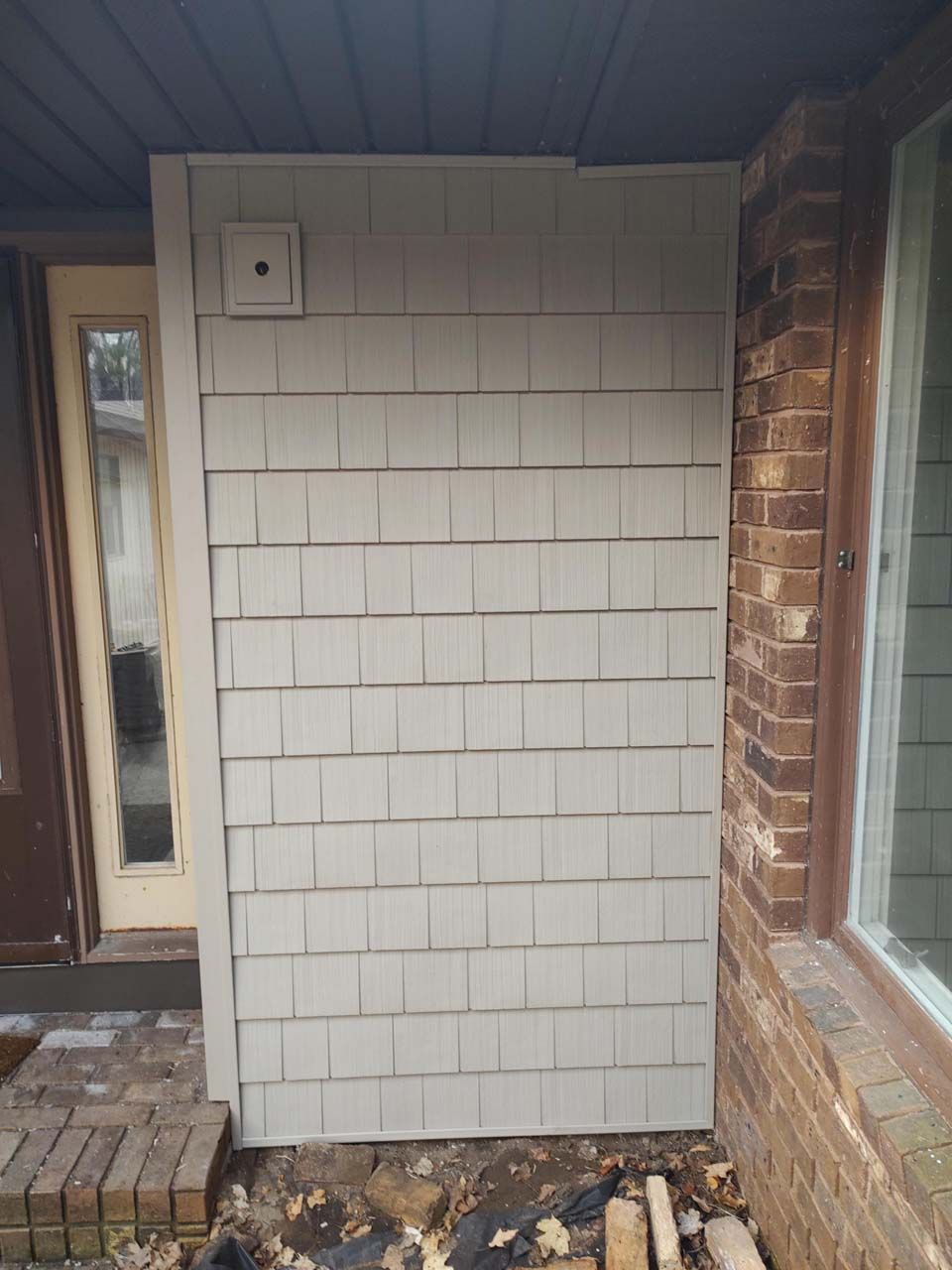 A white siding is being installed on the side of a brick house.