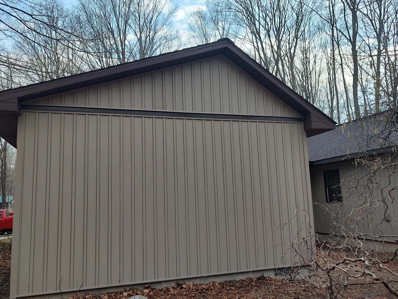 A garage with a brown roof is sitting next to a house in the woods.
