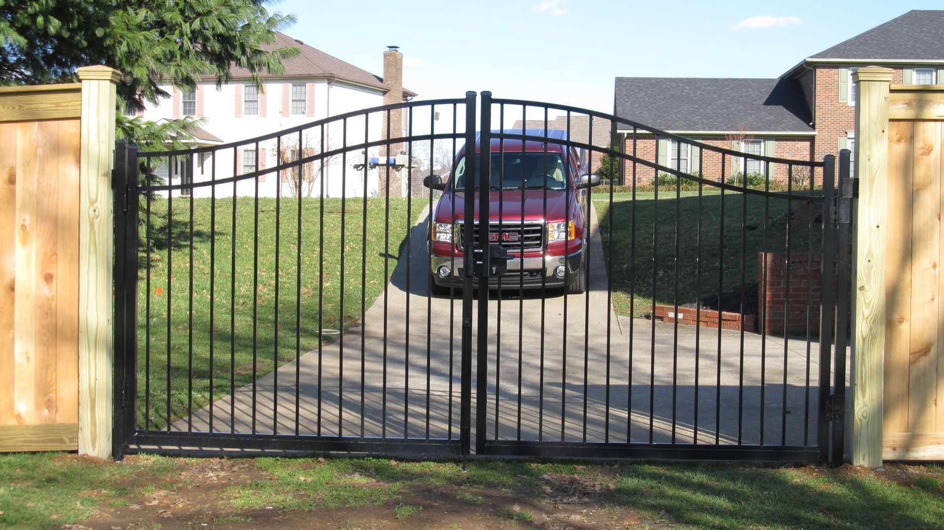 Black metal driveway gate between brick pillars, with a red car parked behind it.