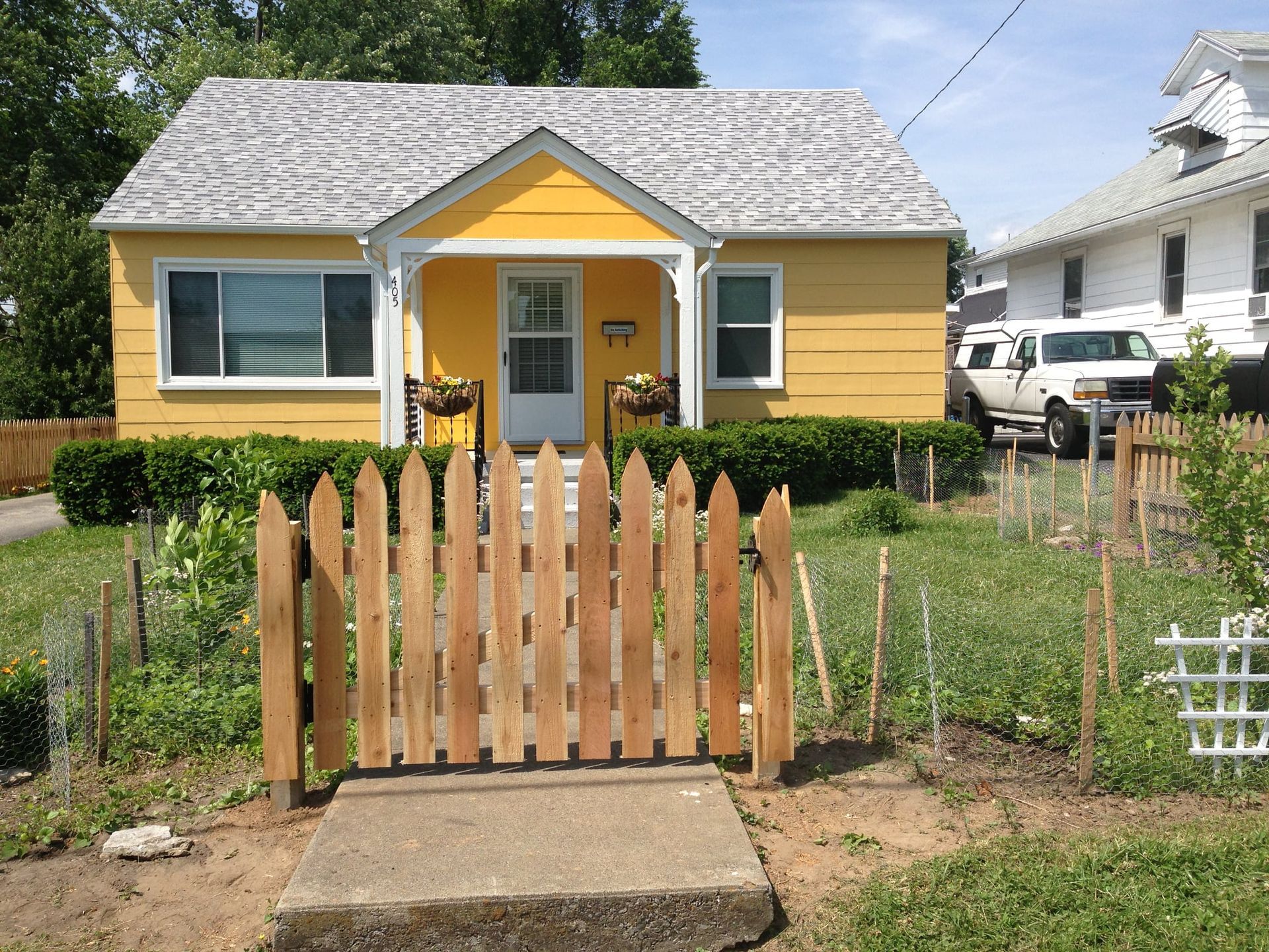 Yellow bungalow with white trim and a wooden gate in front of a small garden